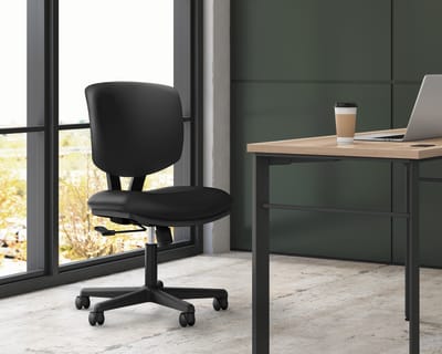 A modern, minimalist office space with a black office chair and a wooden desk near a large window overlooking a natural landscape.