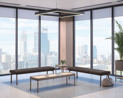 Modern office lounge with two long cushioned benches and a rectangular coffee table, set against floor-to-ceiling windows showcasing a city skyline, accented by a geometric ceiling light and potted plant.