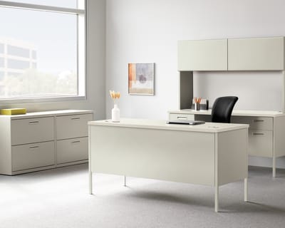 A modern, minimalist office space with a white desk, cabinets, and a framed artwork on the wall, set against a bright, natural light-filled background.