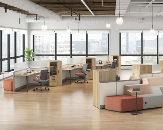 A modern, open-concept office space with cubicles, seating areas, and large windows providing ample natural light.
