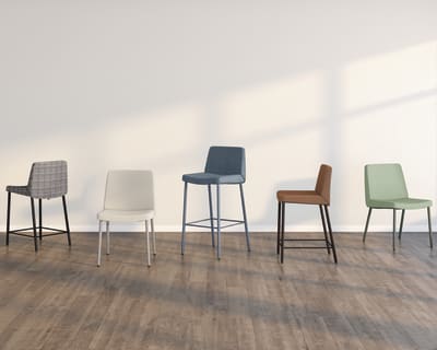 A collection of modern, minimalist bar stools in various colors and designs, arranged on a wooden floor against a plain white wall.