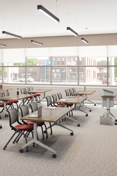 Flexible classroom with movable tables and chairs, large windows, ceiling lights, wall-mounted displays, and instructor podium in a bright, modern space.