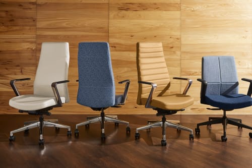 The image shows several office chairs of different designs and colors arranged in front of a wooden wall.