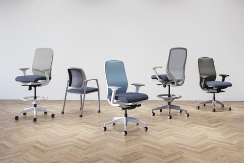 A collection of modern, adjustable office chairs in various shades of gray and blue, arranged on a herringbone-patterned wooden floor against a plain background.