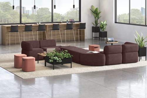 A modern and minimalist lobby or waiting area with comfortable burgundy sofas, potted plants, and a wooden reception desk against a backdrop of large windows overlooking a lush outdoor environment.