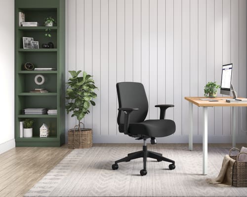 A modern and minimalist home office space with a wooden desk, a black office chair, and a green shelving unit against a white paneled wall.