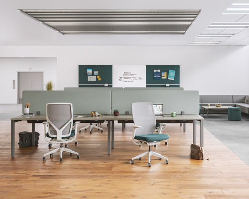 A modern, minimalist office space with a mix of gray and white furniture, including desks, chairs, and storage units, set against a bright, open background.