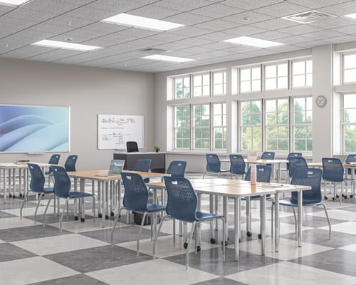 Bright modern classroom with movable tables, blue chairs, whiteboard displays, and large windows bringing in natural light.