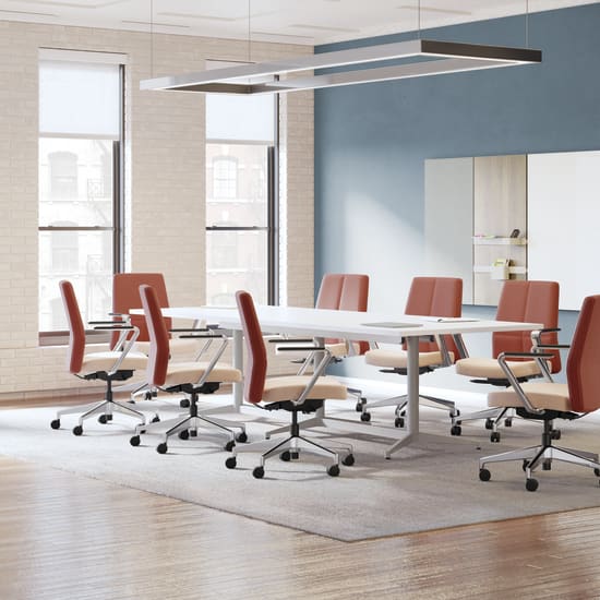 A modern and minimalist conference room with a long wooden table surrounded by red office chairs, a large mirror on the wall, and a sleek lighting fixture overhead.