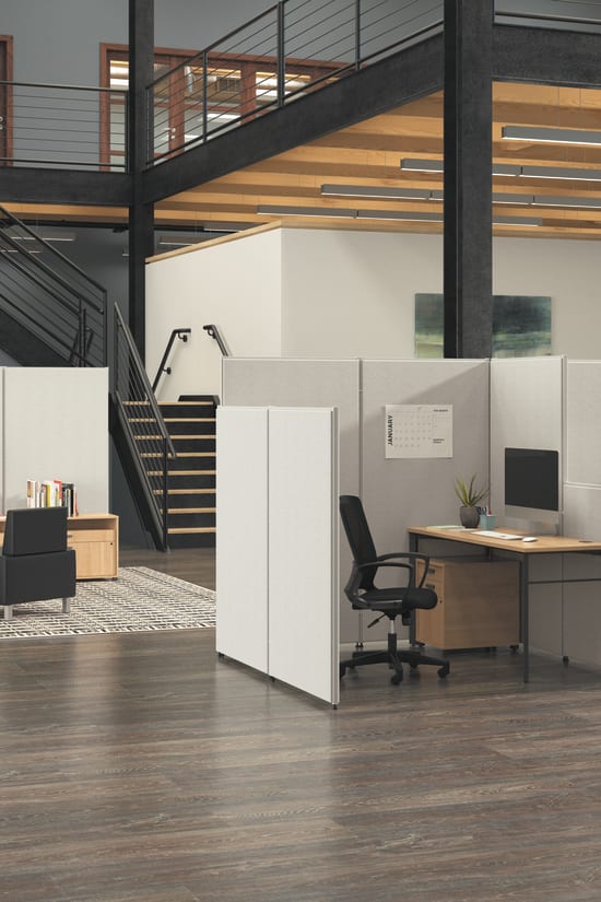 A modern, open-concept office space with a loft-style layout, featuring a mix of workstations, storage units, and a staircase leading to an upper level.