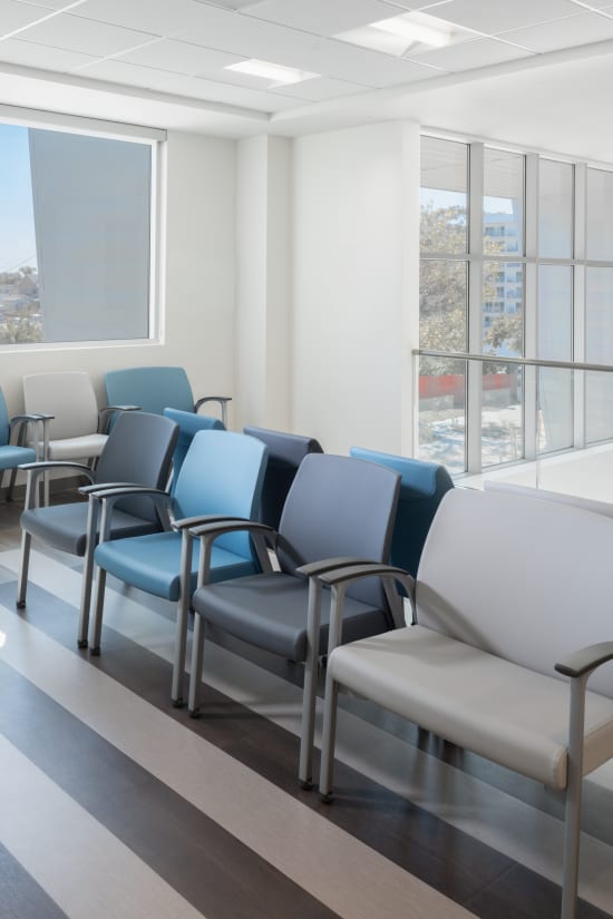 A modern, well-lit waiting room with rows of comfortable chairs and large windows overlooking an urban landscape.