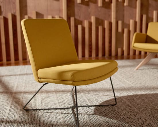 Two yellow upholstered chairs with metal frames sit on a carpeted floor in front of a wooden slatted wall.