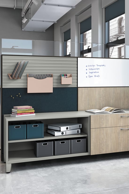 A modern, minimalist office space with a whiteboard, shelves, and storage units, set against a backdrop of large windows and a concrete floor.