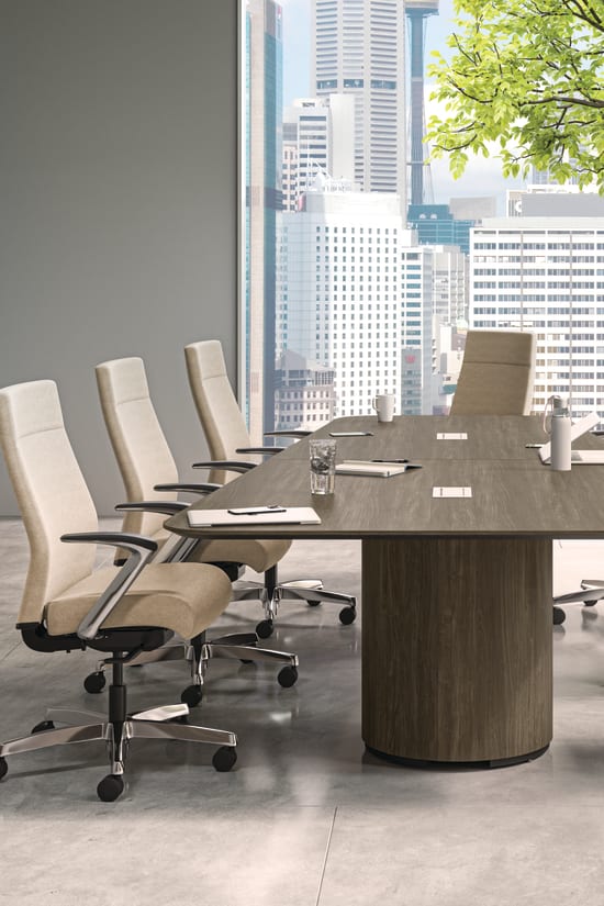 A modern and minimalist conference room with a large wooden table surrounded by white office chairs, overlooking a cityscape through the large windows.