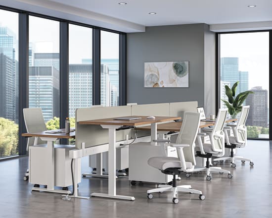 Modern office workspace with height-adjustable desks, ergonomic white chairs, and floor-to-ceiling windows overlooking a city skyline.