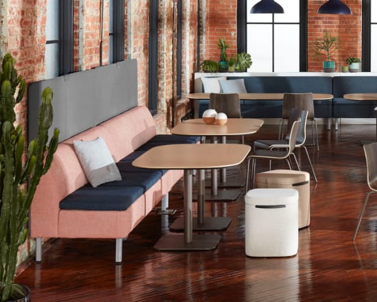 A cozy and modern cafe interior with wooden tables, plush pink seating, and industrial-style lighting fixtures against a backdrop of exposed brick walls.