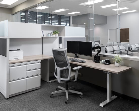 Open workstation with white cubicle panels, light wood desk, and dual monitors.