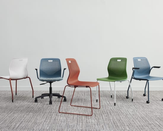 A collection of colorful, modern-looking chairs arranged on a gray tiled floor against a plain white wall.