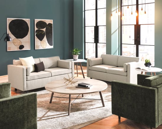 A cozy and stylish living room with neutral-toned sofas, abstract artwork on the walls, and a round wooden coffee table in the foreground, set against a backdrop of large windows and a lush indoor plant.