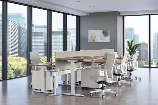 Modern office workspace with height-adjustable desks, ergonomic white chairs, and floor-to-ceiling windows overlooking a city skyline.