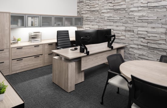 Private office with light wood furniture, dual monitors, black chair, and stone accent wall.