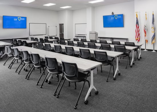 Training room with long tables, black chairs, and dual wall-mounted screens.