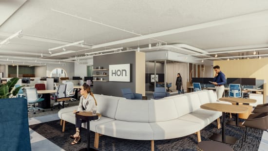 Curved upholstered modular sofa with low profile seating, paired with round wood‑top tables on pedestal bases and small side tables with slim bases.