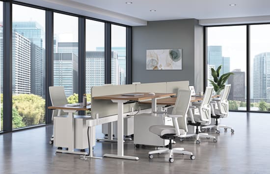 Modern office workspace with height-adjustable desks, ergonomic white chairs, and floor-to-ceiling windows overlooking a city skyline.