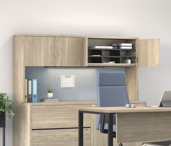 A modern and minimalist home office space with a wooden desk, black chairs, and a storage unit with shelves and cabinets against a gray wall, complemented by potted plants and framed artwork.