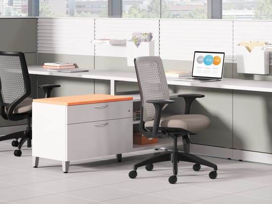 A modern, well-equipped office workspace with a desk, computer, and ergonomic office chair, set against a backdrop of large windows providing natural light.
