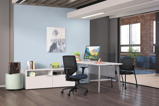 A modern, minimalist home office with a white desk, a computer monitor, and a black office chair, set against a backdrop of exposed brick walls and wooden ceiling beams.