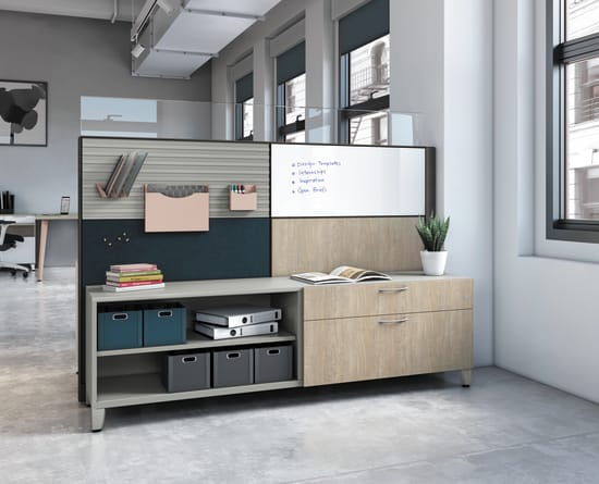 A modern, minimalist office space with a whiteboard, shelves, and storage units, set against a backdrop of large windows and a concrete floor.