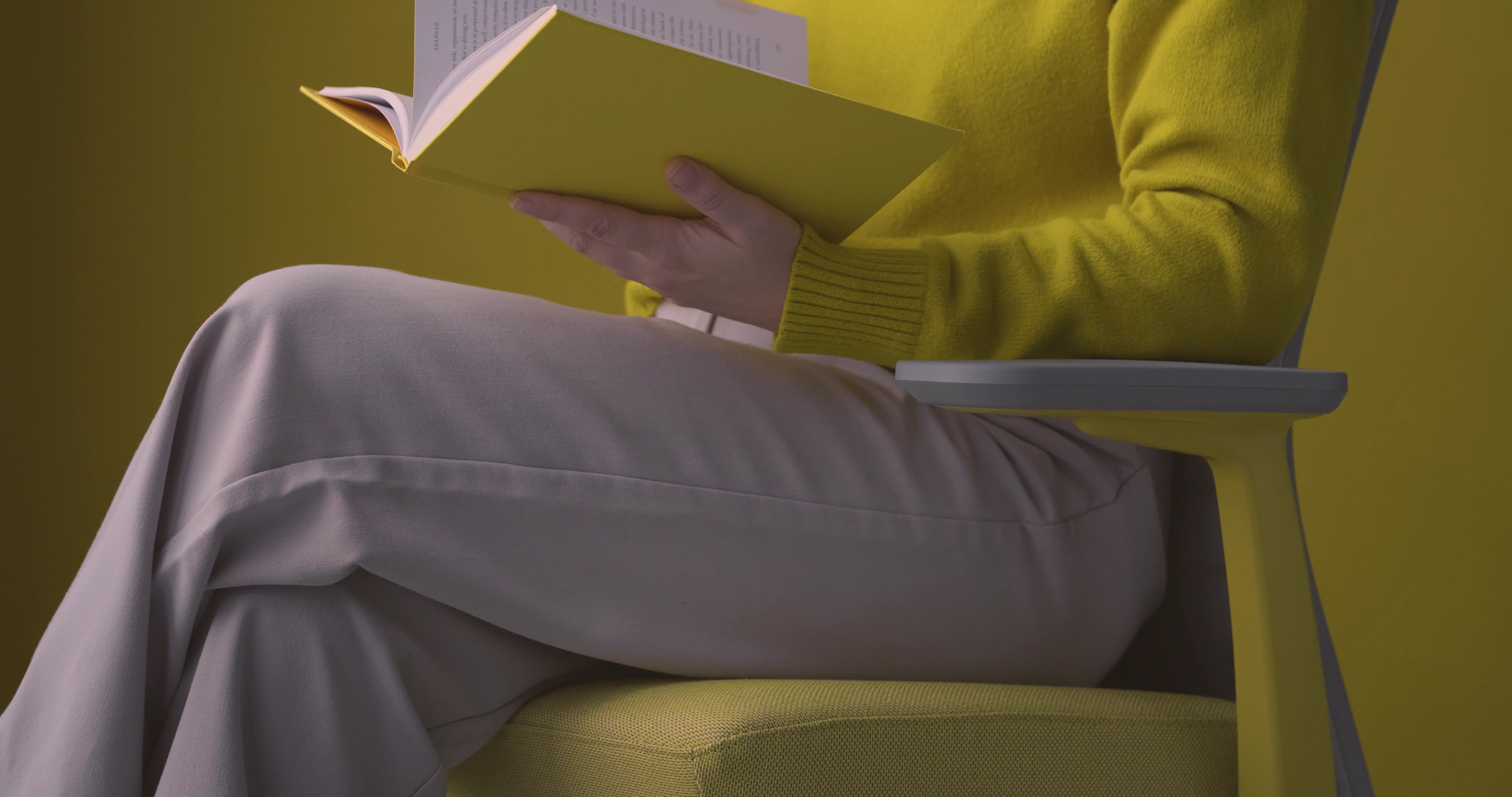Slow motion video of one person reading a book while sitting in a gray and yellow Evo Task Chair in a yellow room
