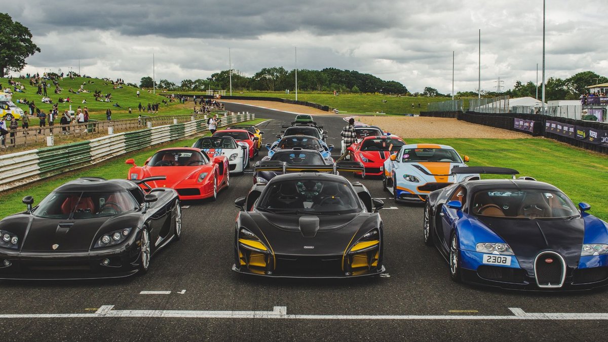 A lineup of luxury sports cars ready for a racing event at an outdoor track.