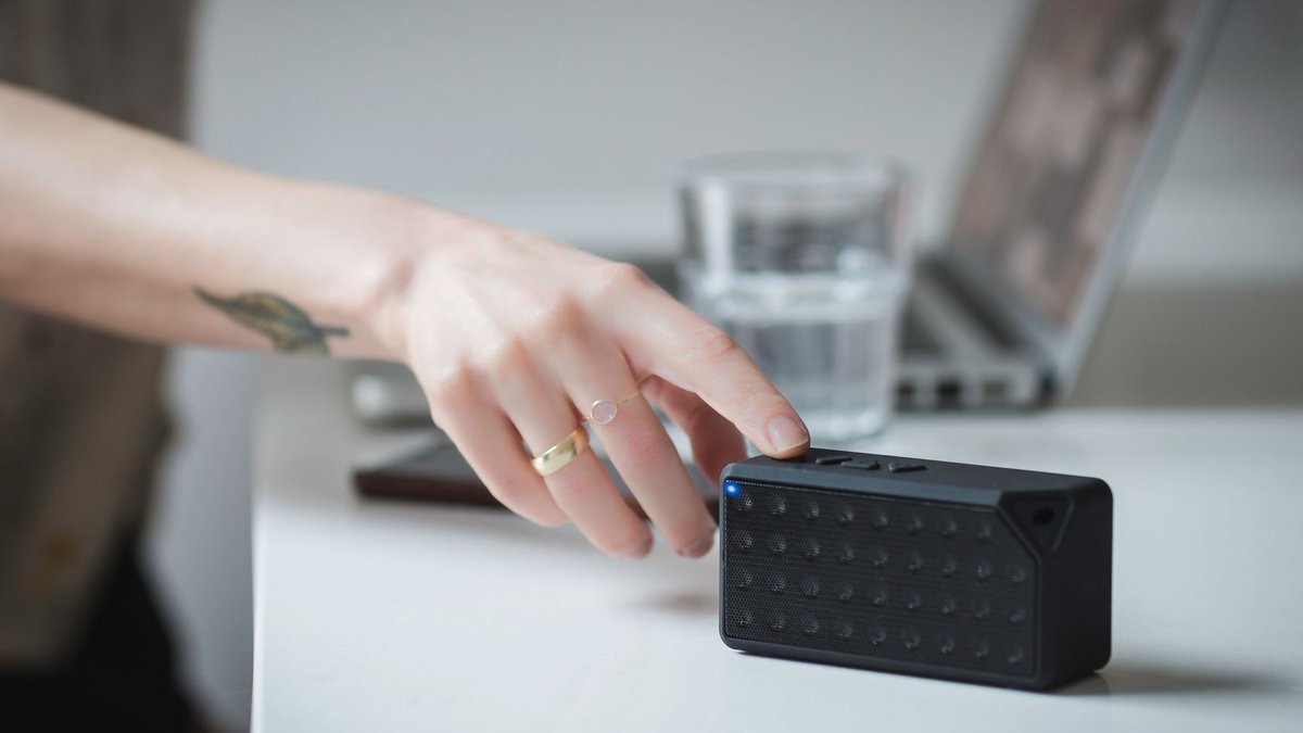 Portable e-readers and accessories gain fans Close-up of a person adjusting a portable Bluetooth speaker on a desk indoors, with a laptop in the background.
