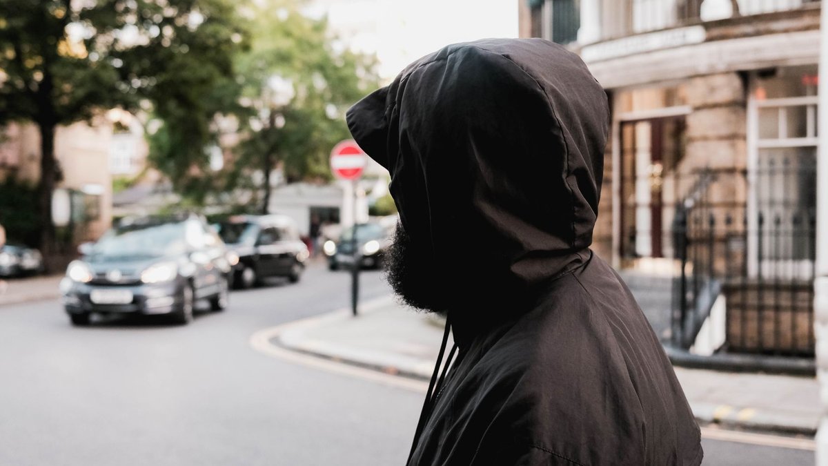 X to reveal post censorship to users Person in black hood standing on a city street corner with traffic.