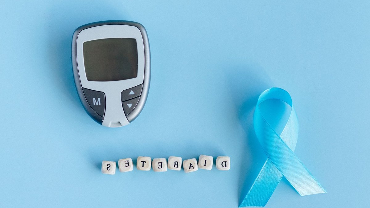 Blue ribbon and glucose meter on blue background highlighting diabetes awareness.