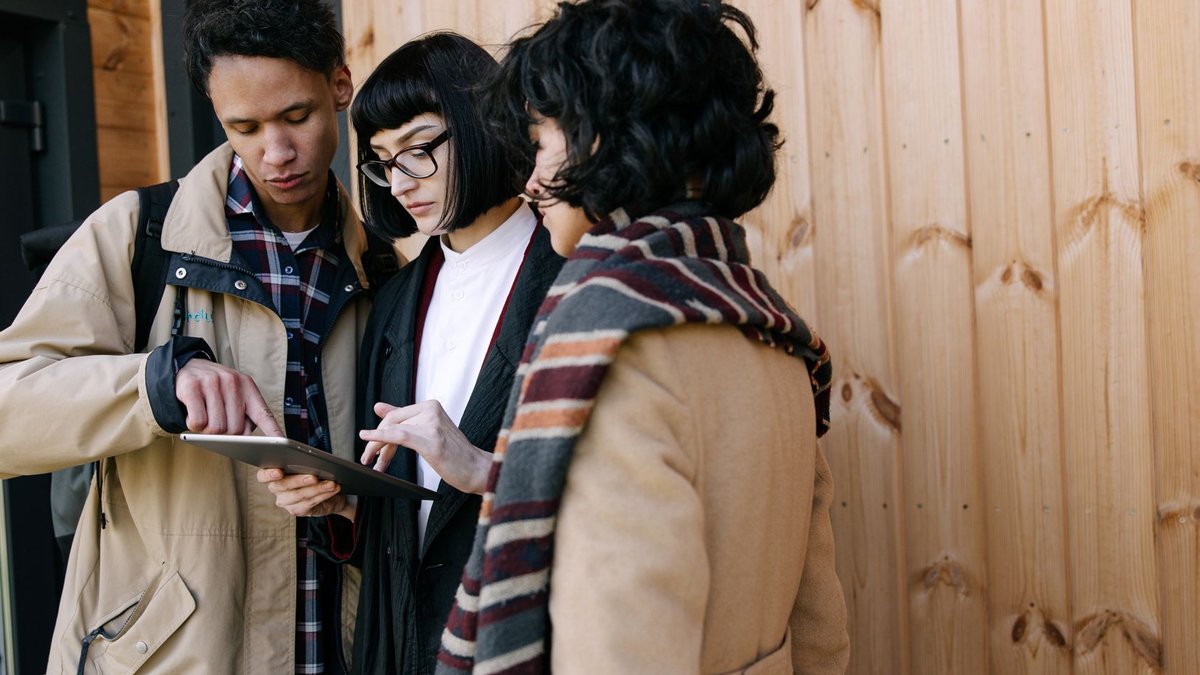 Three adults collaborating using a digital tablet against a wooden wall, possibly real estate agents.
