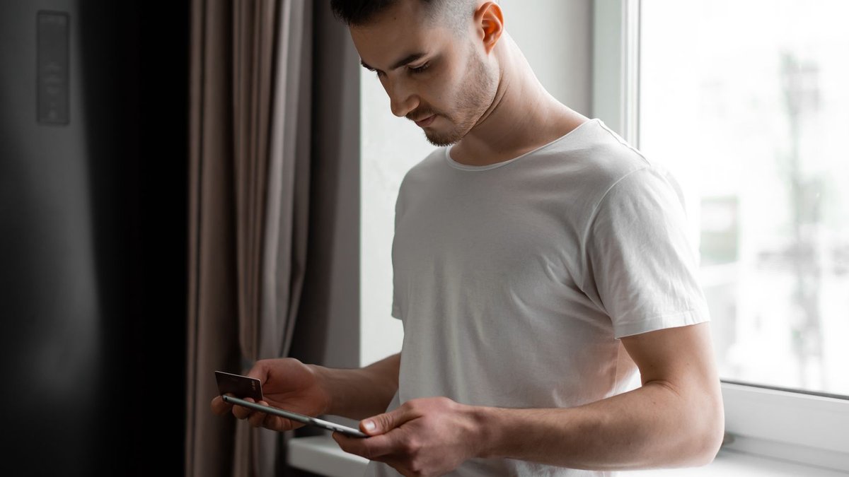 Window Depot of the Gulf Coast Files Chapter 7 Young man standing by a window, using tablet and credit card for online shopping indoors.