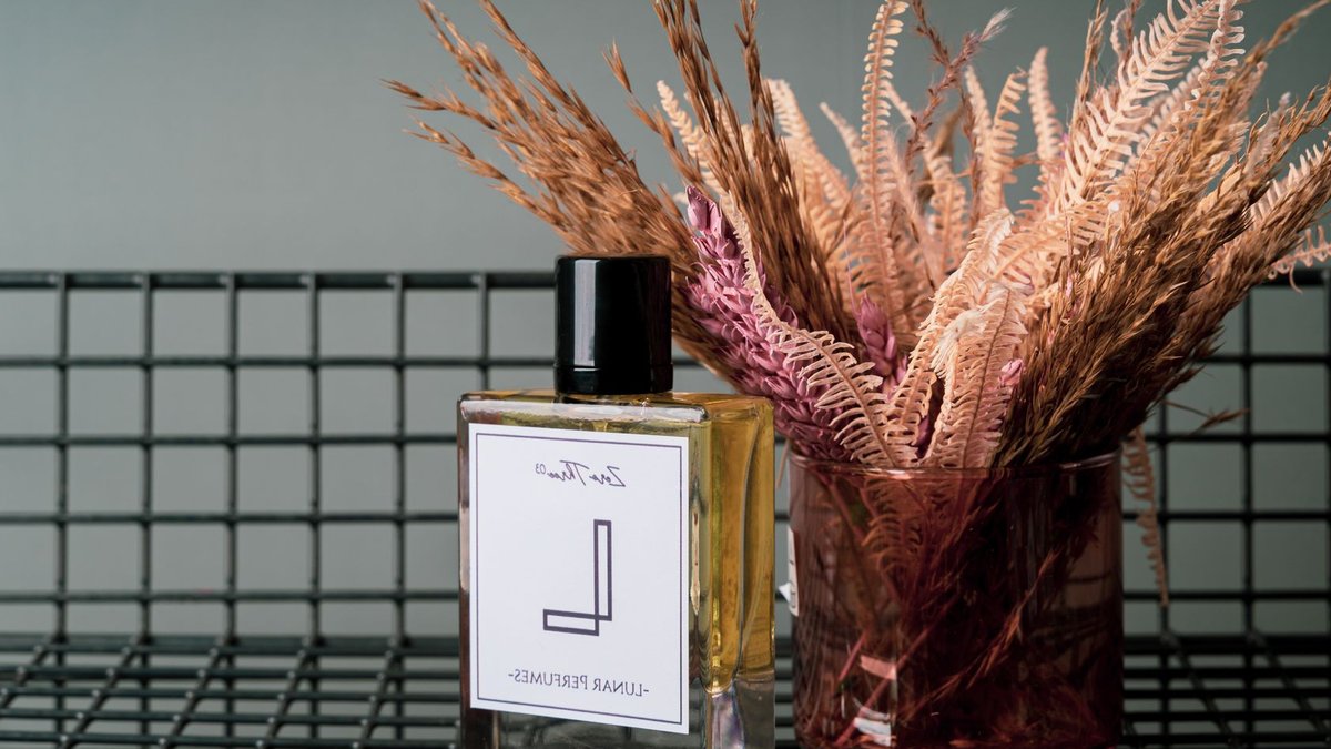 Elegant perfume bottle and dried flowers on a wire grid surface, perfect for luxury and aroma themes.