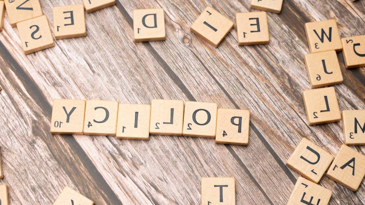 Scrabble letter tiles on a wooden background forming the word "Policy".