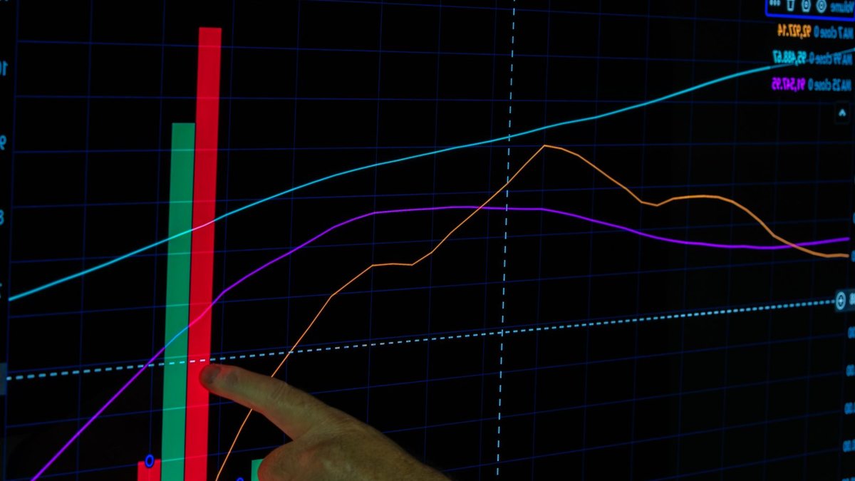 Hand pointing at a financial graph displaying cryptocurrency data analysis and trends.