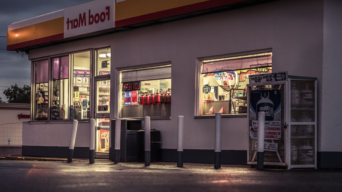 Exterior view of a food mart at night with illuminated signage and bollards.