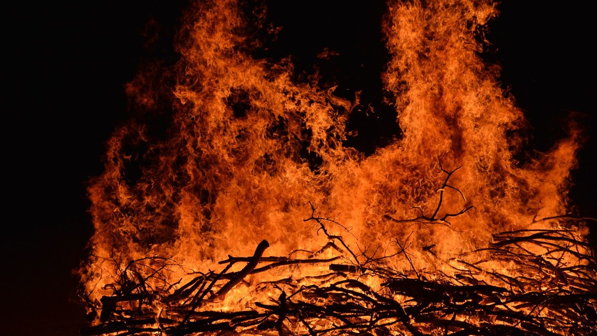 Dramatic close-up of a blazing bonfire with vivid orange flames against a dark night sky.