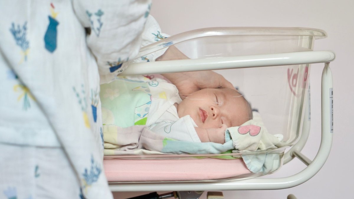 Second opinion leads to successful spinal tumor surgery A tender moment of a newborn baby sleeping peacefully in a hospital bassinet being gently touched by a parent.