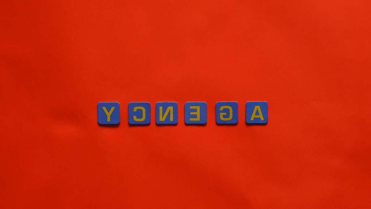 Blue letter tiles spelling 'AGENCY' on a vibrant red background, ideal for creative promotion.