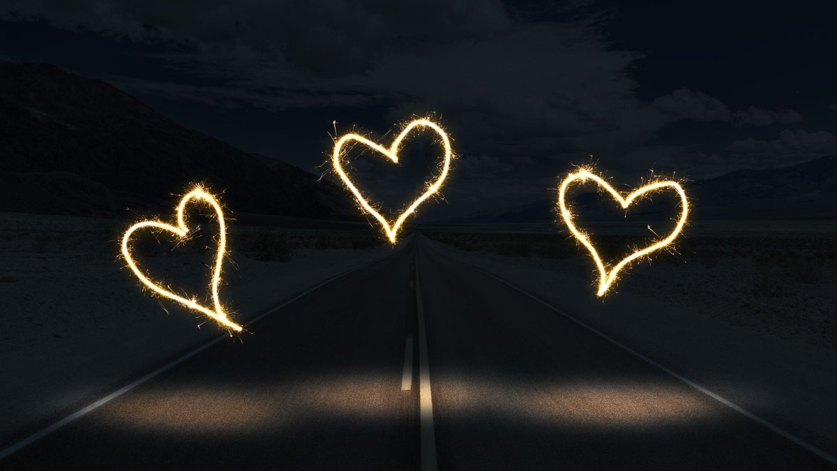 Three illuminated heart shapes created with sparklers over a dark road at night.