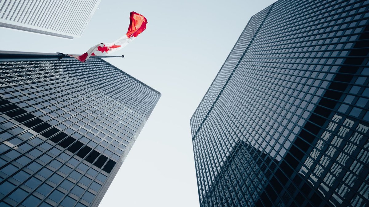 Low angle view of towering skyscrapers and Canadian flag in a modern urban environment.