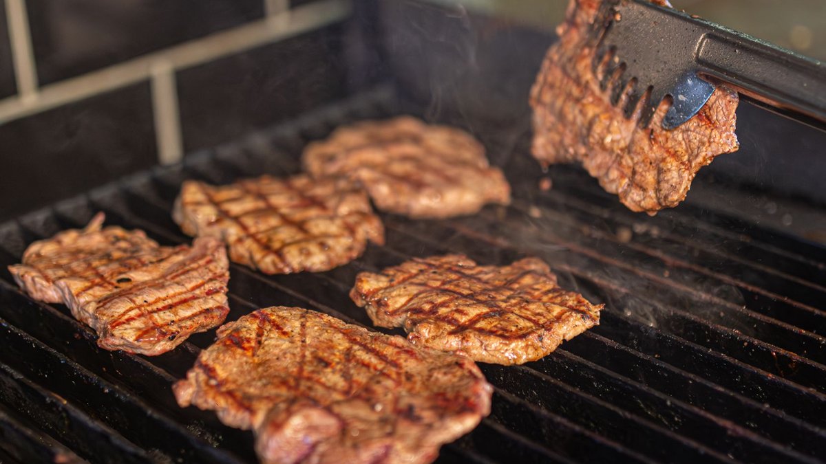 Close-up of juicy beef steaks being grilled, showcasing smoke and grill marks.