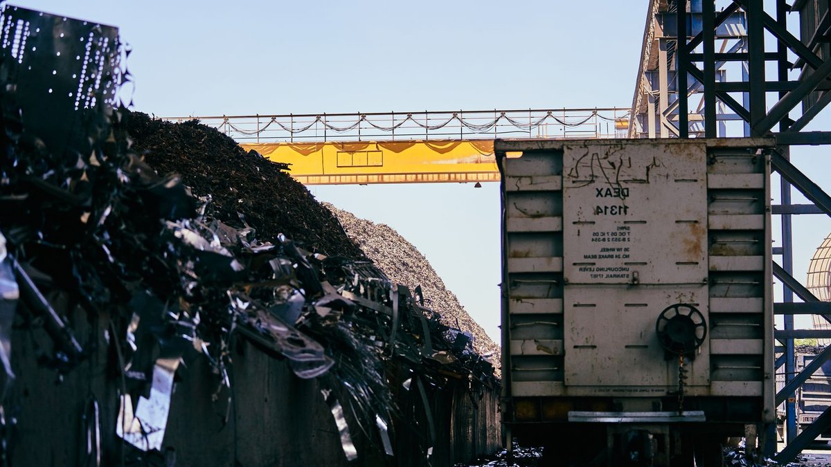 Banten factory expansion boosts chemical production capacity Train car at an industrial scrap metal yard with conveyor belt and metal piles.